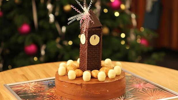 Billedet viser en festlig Klokken-24-kage, pyntet med chokolade som et nytårsur, der slår 12.