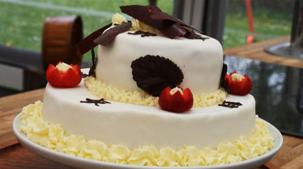 Billedet viser en lagkage overtrukket med hvid fondant og pyntet med chokolade og bær.