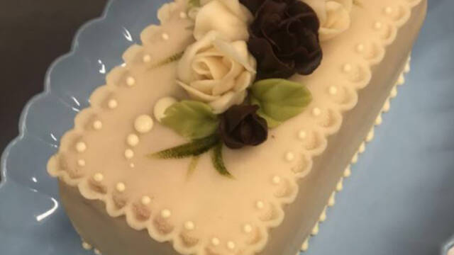 battenberg-kage dekoreret med sort og hvide blomster på blåtfad