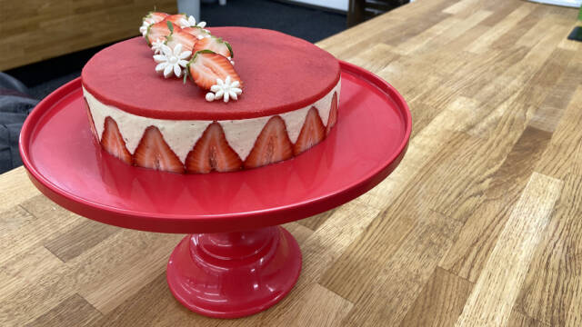 Rød Fraisier-kage pyntet med jordbær, sukkerperler og marcipanblomster.