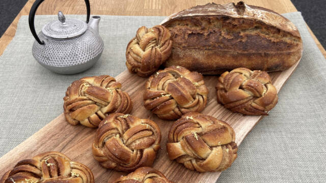Morgenboller og brød på et spækbræt med en tekande i det ene hjørne