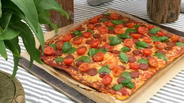 En smuk pizza med tomater, basilikum og pesto