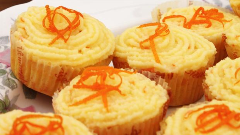 Billedet viser appelsin-cupcakes pyntet med smørcreme og lidt revet appelsinskal.