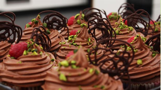 Billedet viser chokolade-cupcakes pyntet med pistacienødder, chokolade og hindbær.