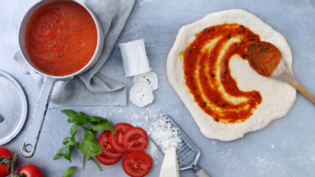 Billede af udrullet hjemmelavet pizzadej, bliver smurt med tomatsovs