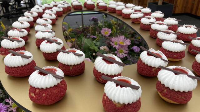 Et bord fyldt med små, runde kager der er røde på siden af bær og har flødeskum og en chokoladestang på toppen.