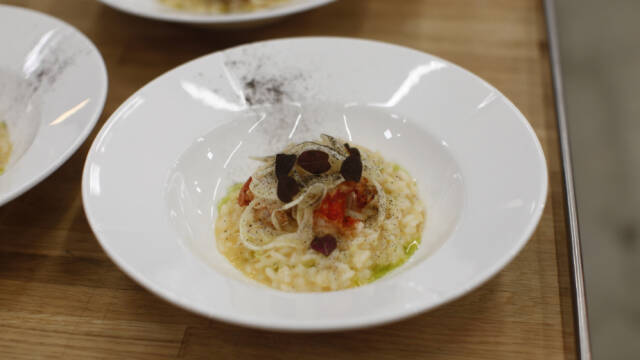 Billedet viser en hvid dyb tallerken med risotto med hummer, fennikel og porre på toppen.