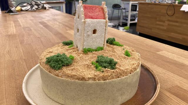 En kage med en kirke på toppen omgivet af sand og buske.